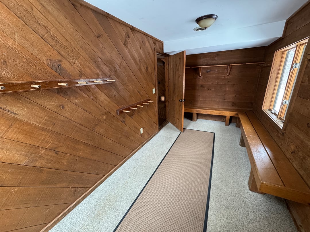 Ski room: Knotty-pine paneled mudroom with long wooden benches, wall ski/pole racks and runner mat
