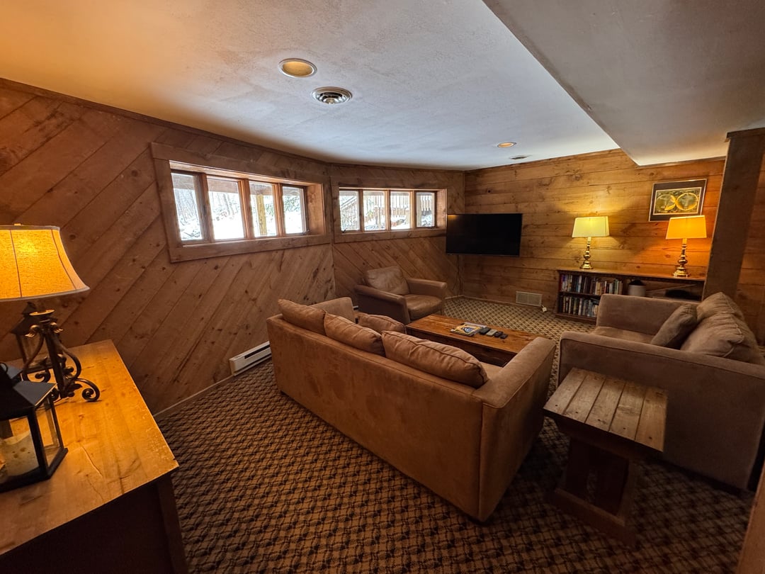 Lower-level den: Suede sofas around a coffee table, TV, clerestory windows, pine paneling, bookshelf