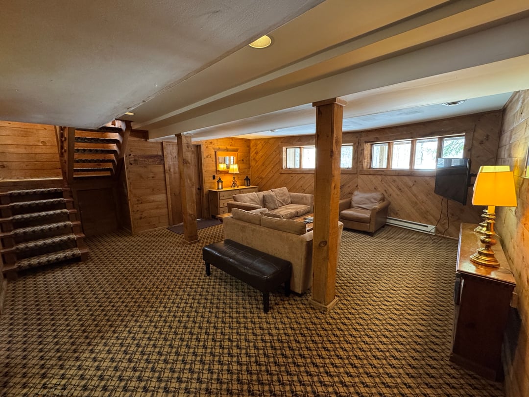 Lower-level den: Wide den view: open-riser stair, sofas, bench, TV and lamp-lit pine walls