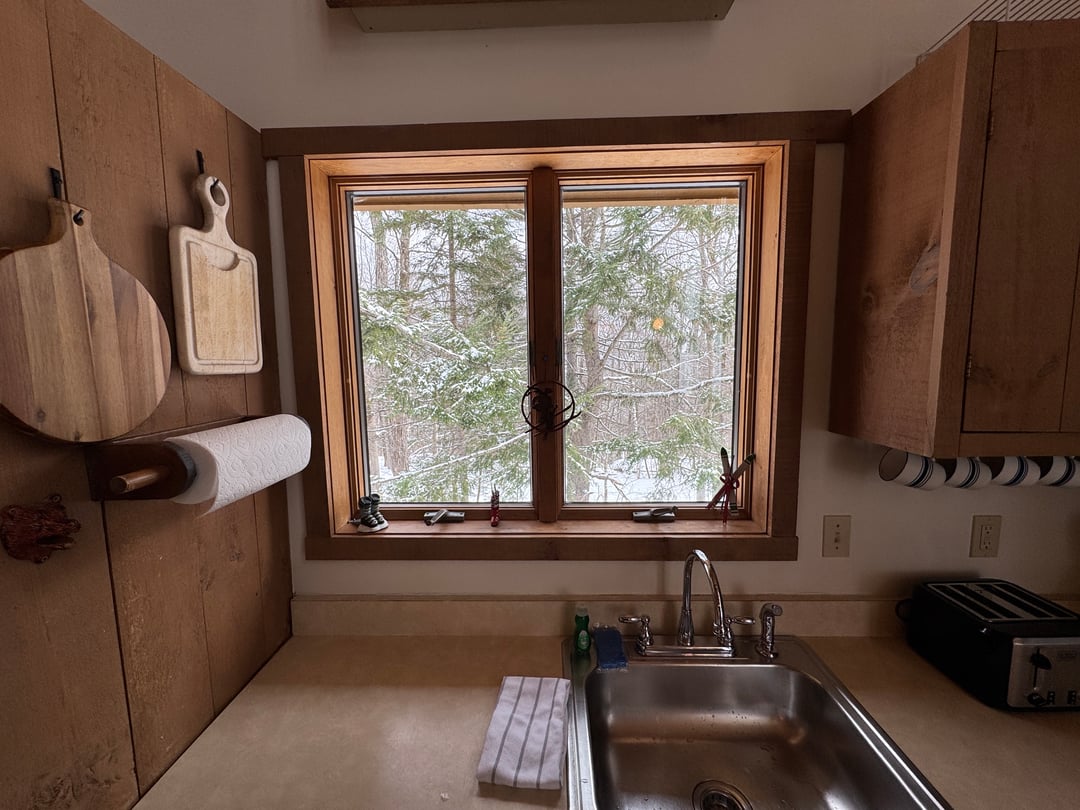Kitchen: Sink under a window framing snowy evergreens, cutting boards on the wall