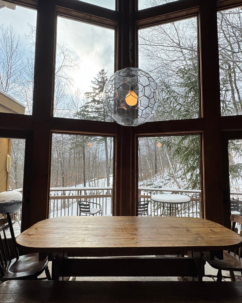 The dining table centered in the two-story window wall, snowy woods and deck outside.