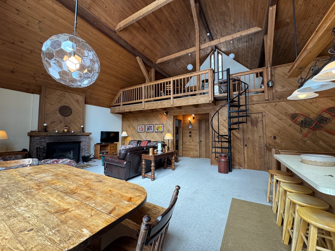 Great room: Wide great-room view from the dining table: exposed beams, loft balcony, spiral stair, kitchen stools
