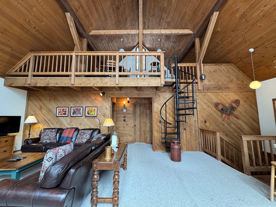Great room: End wall: loft balcony, black spiral stair, leather sofas, snowshoe decor