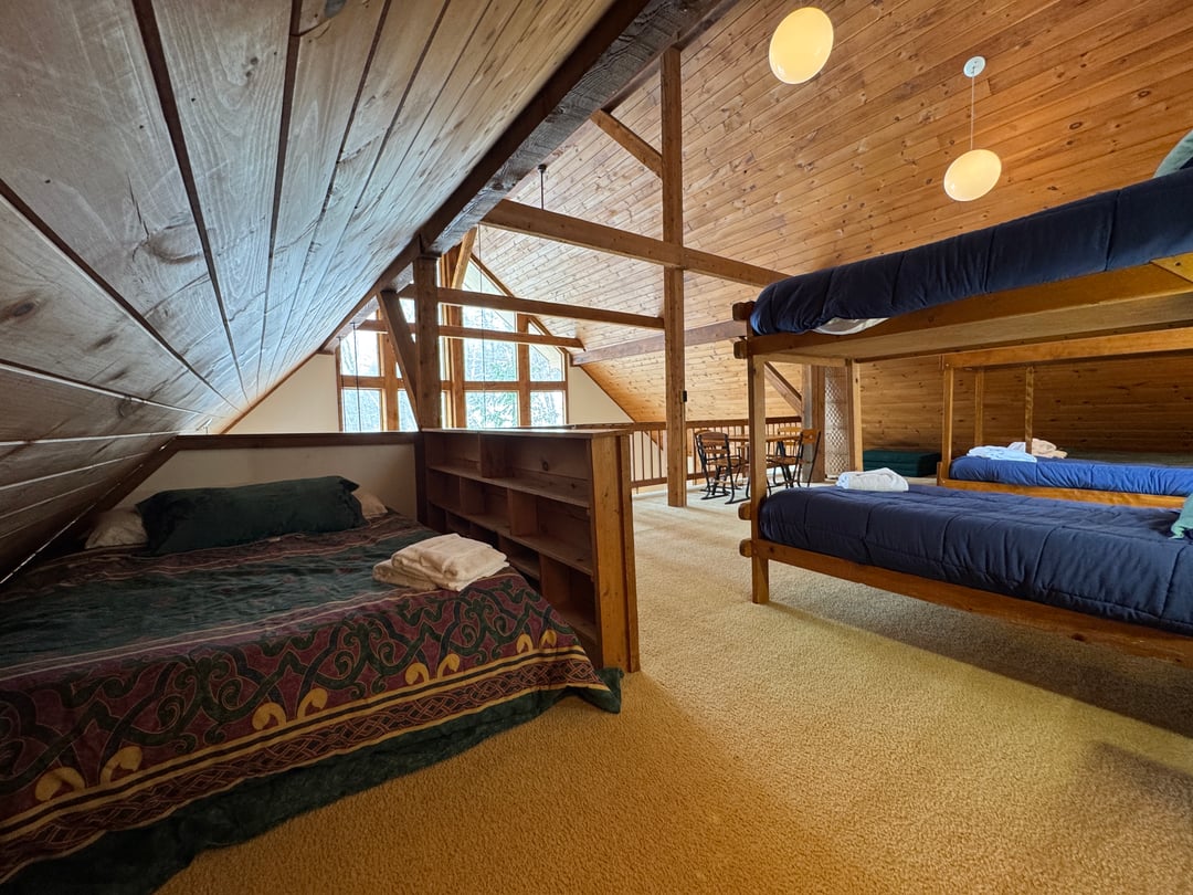 Loft: Queen bed with patterned spread beside a bookcase divider and bunks