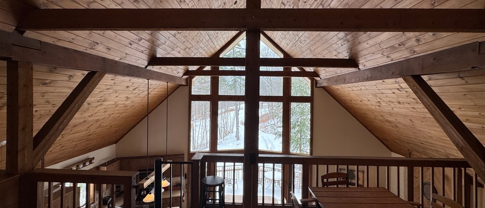 The loft under the ridge: a long table and chairs at the balcony rail, facing the gable window.