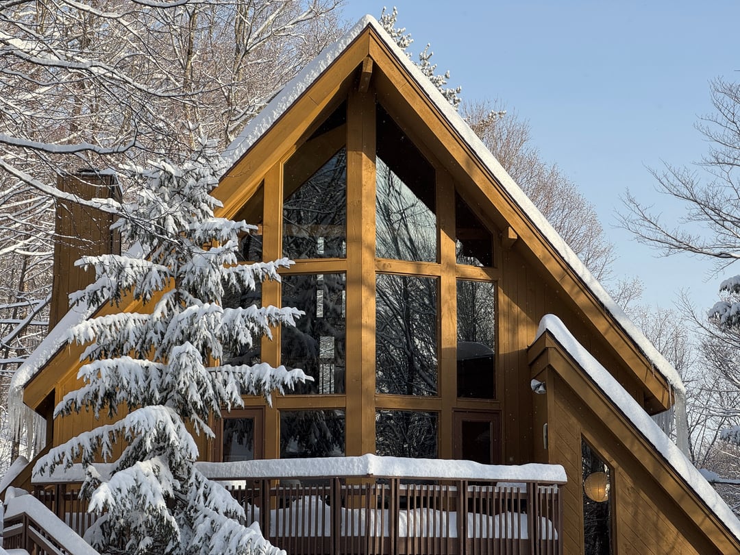 Exterior: Close-up: cedar A-frame with full-height glass, snow-laden spruce, blue sky
